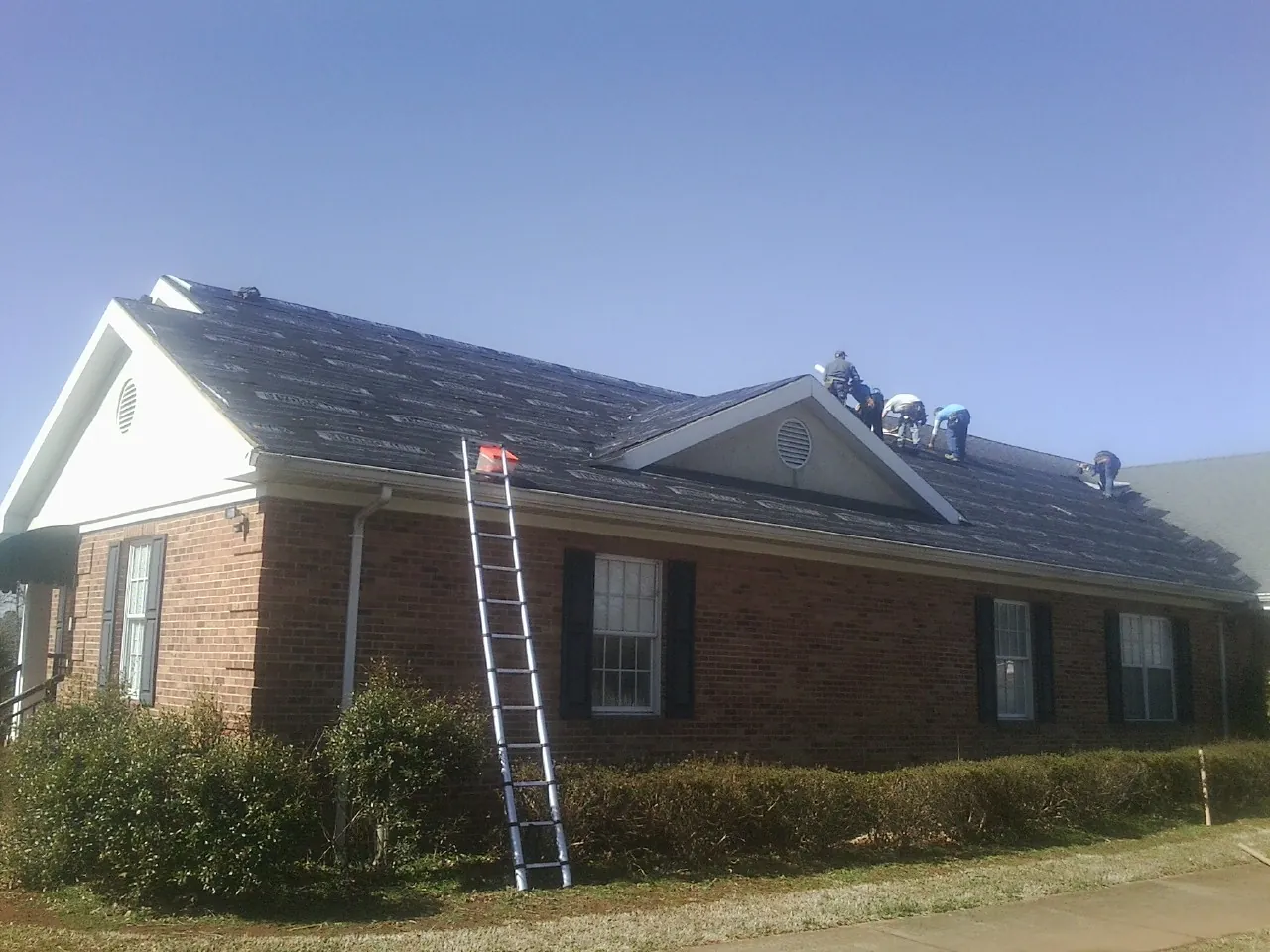 Crew tearing shingles off a brick ranch roof with a ladder set — Metal Roof Repair work by our crew in Dalbo