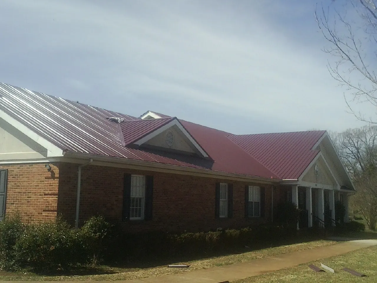 Red metal roof with gabled entries on a long brick building, from a Hail Damage Roof Repair job in Dalbo