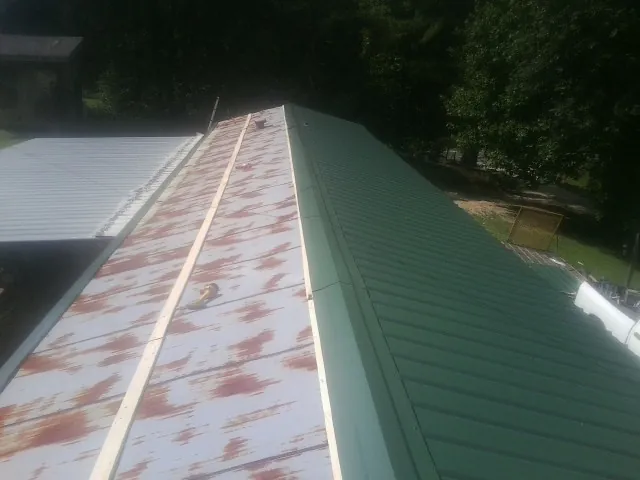 Old rusted panels beside newly installed green metal roofing — Wind Damage Roof Repair by Roofing Brothers in Dalbo
