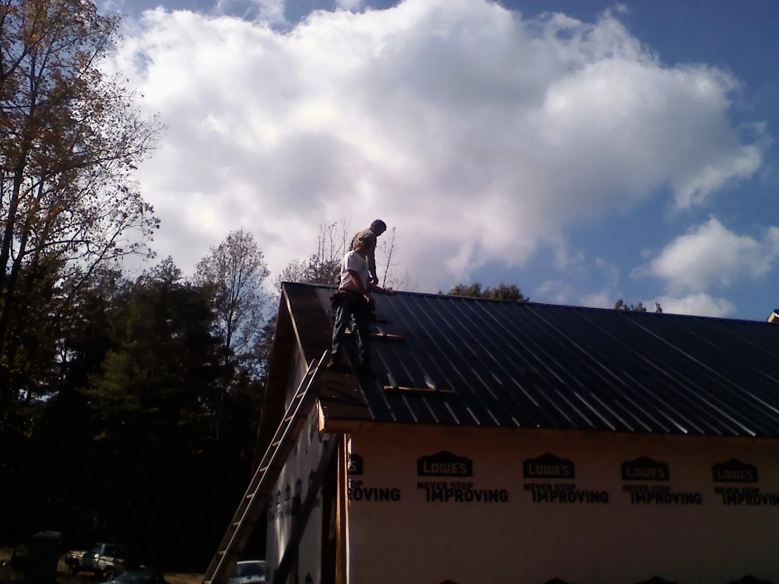 Roofer fastening dark metal panels high against a cloudy sky, from a Roof Inspection job in Dalbo