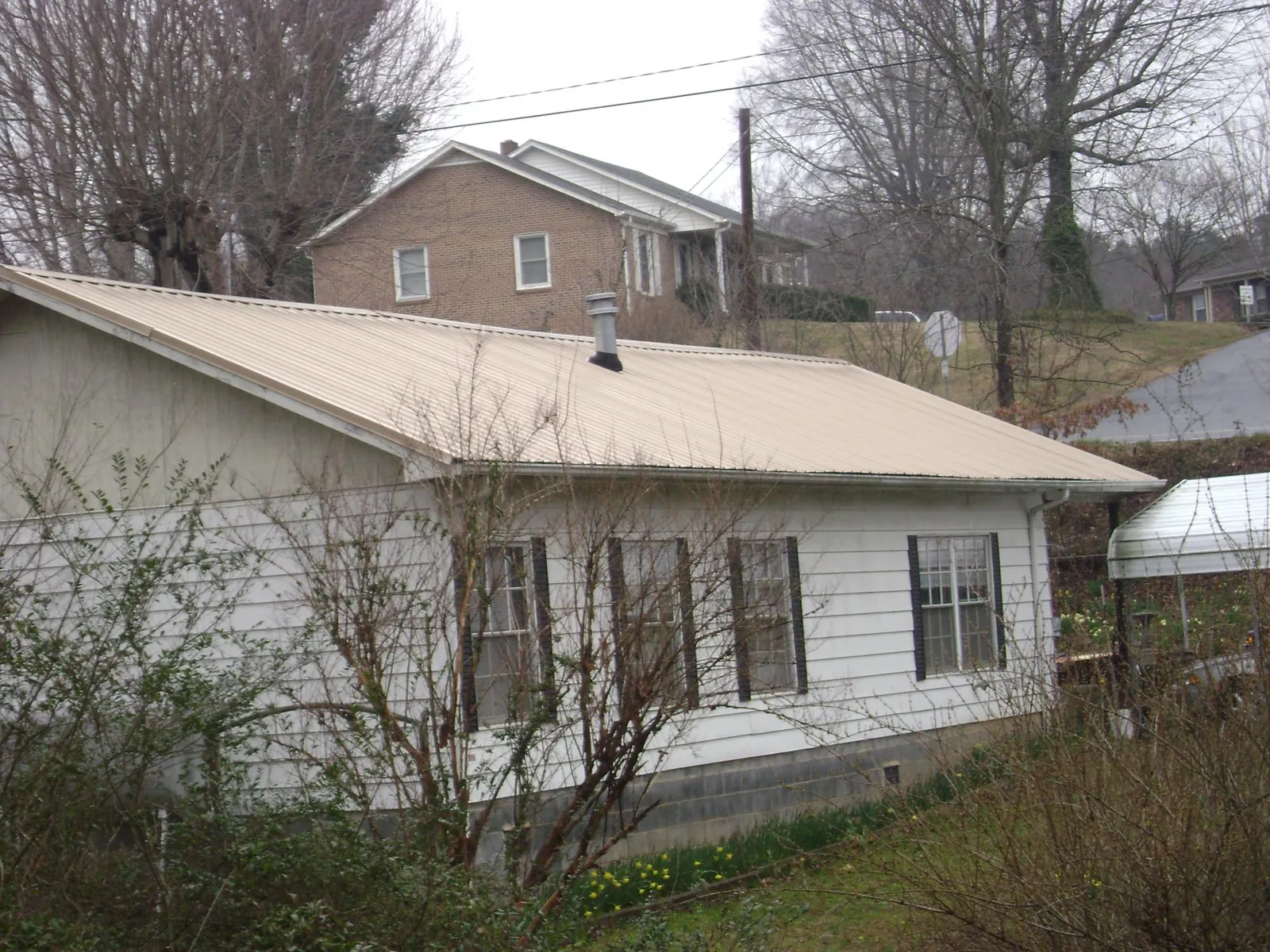 Tan metal roof on a white sided house set into a hillside — Commercial Roofing by Roofing Brothers in Dalbo