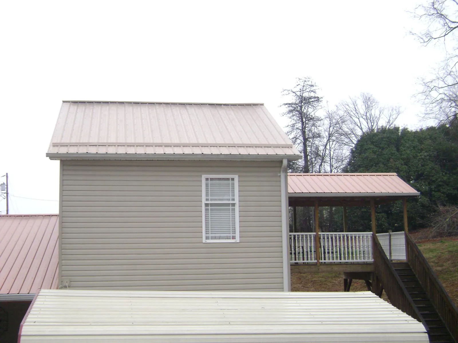 Tan metal roofs on a two story addition and attached porch, from a Roof Replacement job in Dalbo